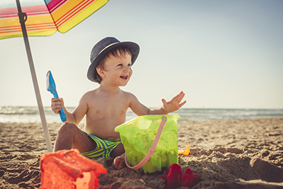 A little boy sits in the shade under an umbrella.