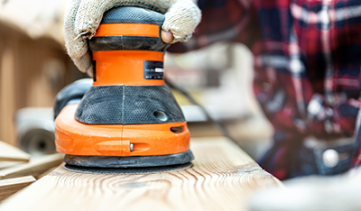 A random orbital sander is used to smooth a piece of lumber.