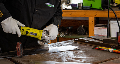 A Forney cup brush is used to remove debris from a piece of metal.